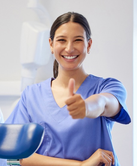 Smiling dental professional giving a thumbs up in a modern clinic setting.