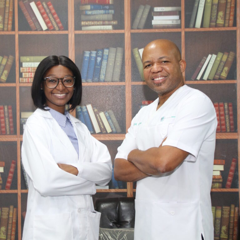 Two smiling dental professionals in white coats standing confidently in front of a bookshelf, representing expertise in dental care at a modern clinic.
